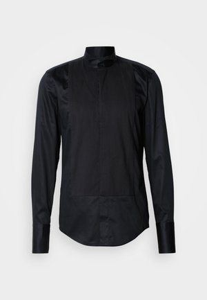 Melna garā piedurkne krekls ar mandarina apkakli, priekšējais panelis ar vertikālām svītrām un gludu tekstūru. Aprīkots ar pogu aizdari.