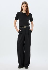 Sort kortærmet t-shirt parret med højhævede sorte bukser med vide ben og et grønt bælte med en guldbuckle.