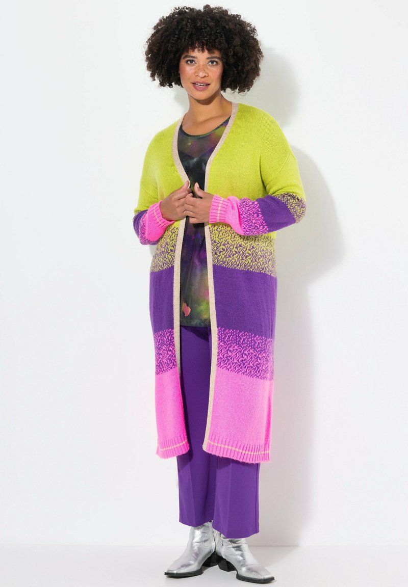 Long cardigan dans des couleurs vives de vert, violet et rose en blocs ; matériau en tricot doux avec des poignets côtelés et une bordure beige.