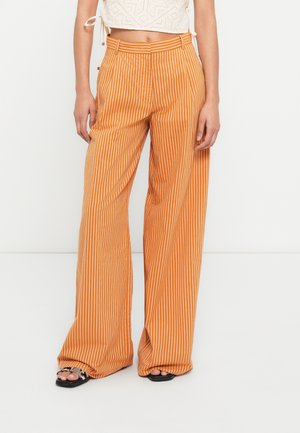 Pantalon à jambes larges orange avec des rayures verticales blanches. Il présente une taille haute avec des passants pour ceinture et un tissu texturé.