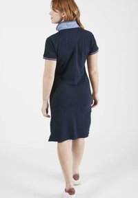 Robe polo marine à manches courtes, col à motif floral et bordures contrastantes. Tissu doux avec une coupe droite, atteignant juste au-dessus du genou.