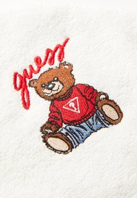 Embroidered patch of a bear in a red sweater and blue jeans on a white, textured fabric background, with "guess" in red above.