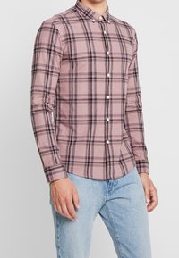 Koszula w drobną kratę z długim rękawem w jasnoróżowym kolorze z czarno-białym wzorem w kratę, kołnierzyk zapinany na guziki i białe guziki. Casualowy krój.