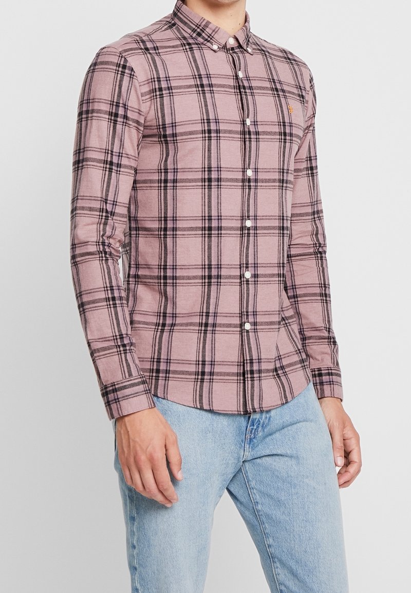 Koszula w drobną kratę z długim rękawem w jasnoróżowym kolorze z czarno-białym wzorem w kratę, kołnierzyk zapinany na guziki i białe guziki. Casualowy krój.