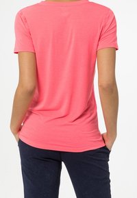 Pink short-sleeve t-shirt with a round neckline and a smooth texture, paired with dark pants, viewed from the back.