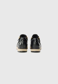 Des chaussures en cuir noir à la finition lisse, avec un bout arrondi et une semelle intermédiaire beige. Des accents en métal doré à l'arrière.