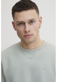 Világoszöld pamut pulóver bordázott kerek nyakkal, kis hímzett logóval a mellkason és texturált felülettel.