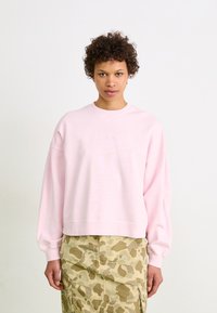 Felpa rosa chiaro con scollo tondo, maniche larghe e polsini a coste, abbinata a una gonna khaki decorata con tasche.