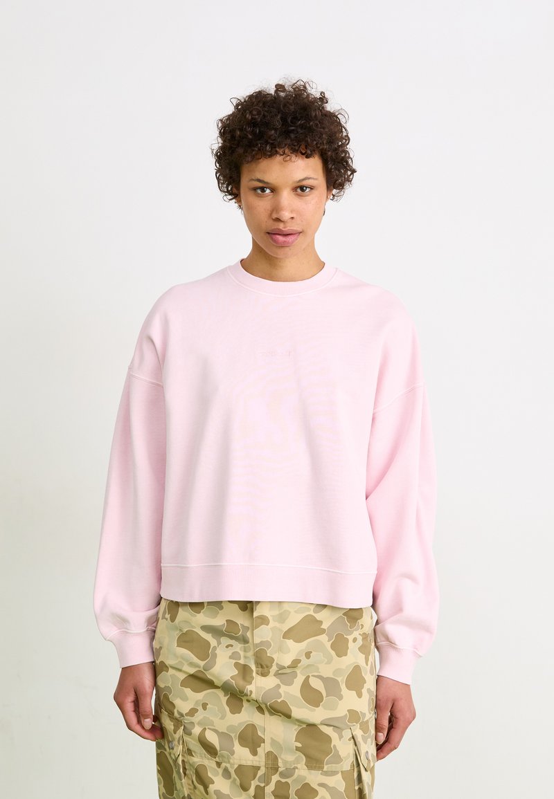 Felpa rosa chiaro con scollo tondo, maniche larghe e polsini a coste, abbinata a una gonna khaki decorata con tasche.