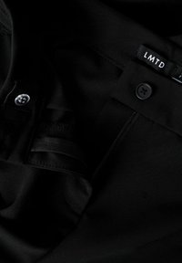 Mustad püksid nööbiga vööl, osaliselt lahtise tõmbluku ja kangast sildiga, millel on kirjas "LMTD", vöö siseosas.