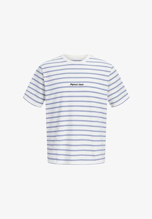 Garçon blond debout, portant un t-shirt rayé blanc et bleu, un pantalon cargo noir et des baskets blanches sur un fond clair uni.