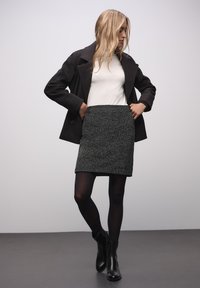 Musta villa-sekoite takki, valkoinen istuva paita ja tekstuuroitu harmaa hame. Mustat sukkahousut ja nilkkurit täydentävät asun. Minimalistinen muotoilu.