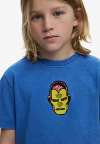 Blue cotton t-shirt featuring an embroidered Iron Man face in yellow and red, with black accents. Short sleeves and crew neck design.