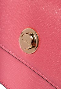 Bolso de mano sintético texturizado en color rosa con un candado circular dorado que presenta el logo de la marca y costuras en negro que contrastan a lo largo de los bordes.