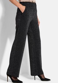 Zwarte glinsterende wijde broek met een elastische tailleband en zijzakken, gecombineerd met zwarte puntige hakken.