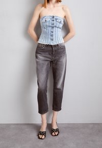 Top in denim blu senza spalline con bottoni frontali, abbinato a jeans grigi a vita corta. Sandali neri con dettagli in metallo completano l'outfit.