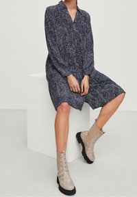 Mörkblå klänning med ett bladmönster, långa ärmar och en knappstängning i halsen, parat med beiga vävda ankelskor med svarta sulor.