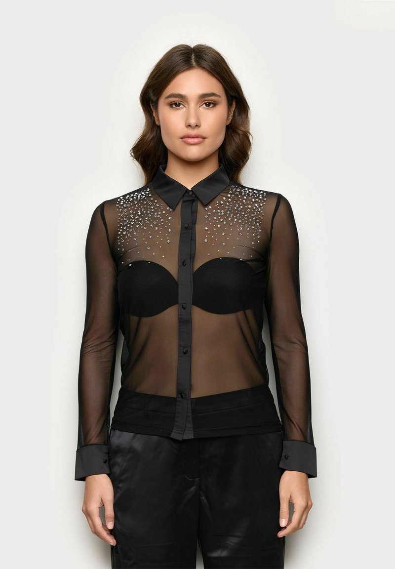 Schwarzes, durchscheinendes Hemd mit langen Ärmeln, das mit dekorativen Strasssteinen im oberen Bereich verziert ist und ein passgenaues schwarzes Oberteil darunter hat.