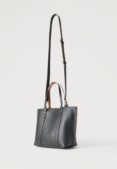 Μαύρη δερμάτινη τσάντα με δύο κοντές λαβές και ένα μακρύ ρυθμιζόμενο λουρί ώμου σε λευκό φόντο.