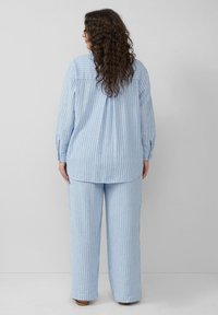 Lichtblauw gestreept loungeoutfit bestaande uit een top met lange mouwen en losse broek. Het materiaal lijkt zacht met verticale witte strepen en heeft een ontspannen ontwerp.