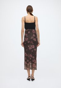 Gjennomsiktig, mørk brun skjørt pyntet med rosa blomster. Midtlengde design med bølget kant, kombinert med en svart, figurnær topp.