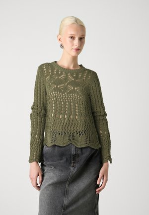 Pull en maille vert olive avec design ajouré, manches longues et ourlet festonné. Porté sur une jupe en denim grise pour un contraste.