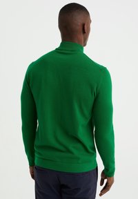 Pull-over moulant vert avec un col haut. Fabriqué en matière tricotée douce. Texture lisse et détails côtelés aux poignets et à l'ourlet.