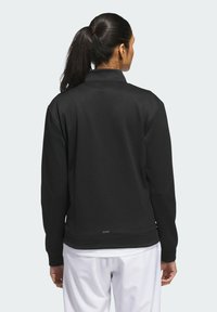 Black sweatshirt with a high collar, made from smooth fabric, featuring long sleeves and a fitted bottom, seen from the back.