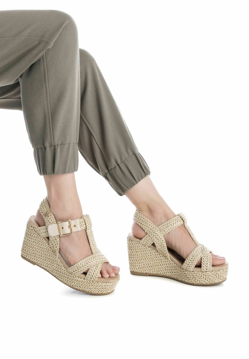 Sandali wedge intrecciati beige con design a fascetta incrociata e fibbia regolabile, caratterizzati da una finitura testurizzata e una suola con piattaforma rialzata.