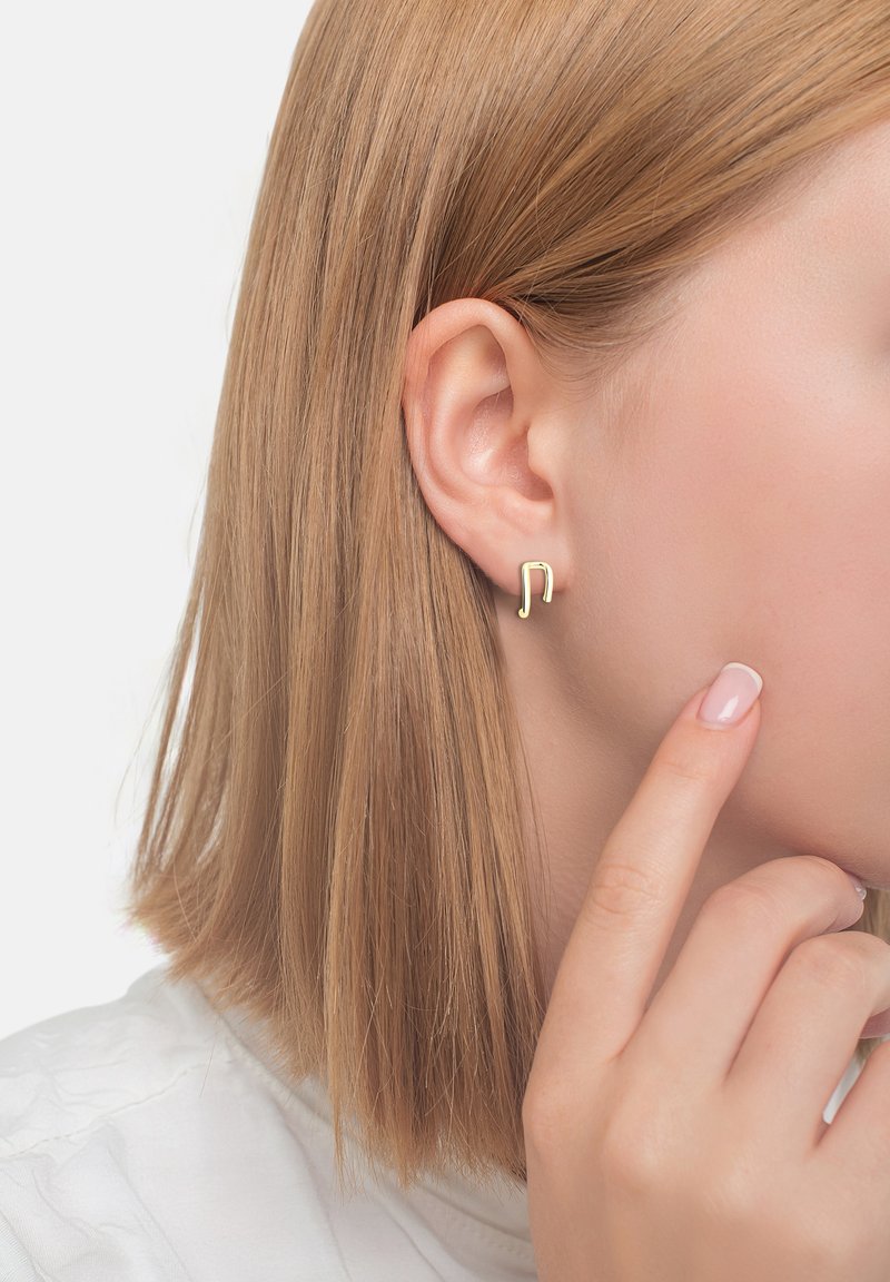 Orecchini a forma di nota musicale dorati, design minimalista, a forma di nota di un quarto, indossati da un modella con capelli biondi e lisci.