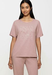 Różowa bawełniana koszulka z luźnym krojem, okrągłym dekoltem i krótkimi rękawami. Z przodu ozdobiona białym wzorem w kształcie kwiatów.