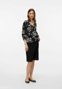 Haut wrap noir à fleurs avec des manches trois-quarts, associé à un short texturé noir et des ballerines noires avec un motif tissé subtil.