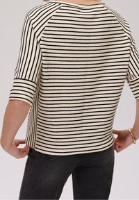 Striped top with three-quarter sleeves, featuring horizontal black stripes on a cream background, textured fabric, and a straight hemline.