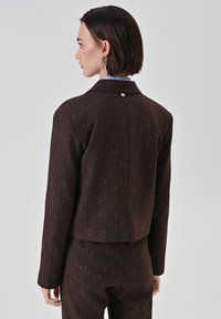 Braune, maßgeschneiderte Jacke mit dezentem senkrechtem Nadelstreifenmuster. Der Stoff hat einen leichten Glanz. Verfügt über einen Reverskragen und eine Knopfdetail auf der Rückseite.