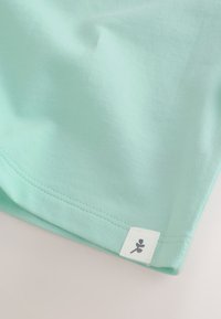 Coin de tissu turquoise clair avec couture double et petite étiquette blanche portant un simple logo plante noir.
