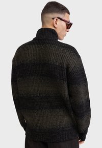 Pull en tricot flou avec un col montant, présentant des rayures horizontales vert foncé et noires, un ourlet côtelé et un tissu texturé.