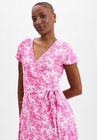 Pink floral wrap dress with short sleeves, V-neck, and a tie at the waist, featuring a textured fabric with a soft, flowy design.