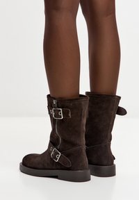 Ghete maro din piele întoarsă, cu fermoar lateral, catarame metalice și talpă plată din cauciuc. Designul include manșete pliate în partea de sus.