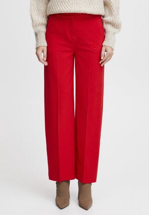 Woman wearing bright red wide-leg trousers paired with beige pointed-toe ankle boots and a cream chunky knit sweater.