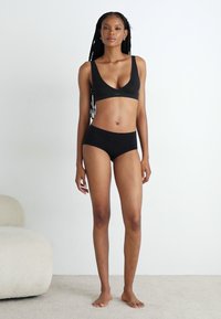 Black bra with a V-neck design and matching black briefs. Smooth fabric with a seamless finish, displayed on a standing figure against a light background.