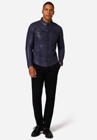 Marinblus av läder med knäppning, två bröstfickor, långa ärmar, slim fit, kombinerad med svarta byxor och svarta skor.