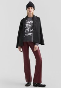 Zwarte pinstripe blazer, grafisch grijs T-shirt, kastanjebruine nep leren flared broek, zwarte enkellaarsjes en een zwarte gebreide beanie.