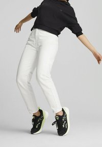 Jeans rectos blancos combinados con una sudadera corta negra y zapatillas negras con acentos de neón. Tela suave con un diseño minimalista.