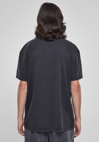 Tricou din bumbac negru cu o croială lejeră, mâneci scurte și decolteu rotund. Detaliu de cusătură vizibil pe margini și la tiv.