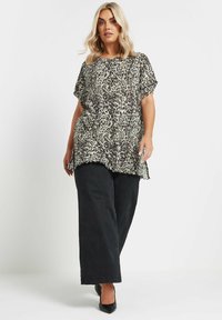 Top de leopardo con mangas cortas, tejido ligero, escote redondo, corte holgado, combinado con pantalones anchos negros y zapatos de punta negros.