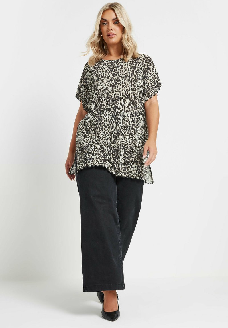 Top de leopardo con mangas cortas, tejido ligero, escote redondo, corte holgado, combinado con pantalones anchos negros y zapatos de punta negros.