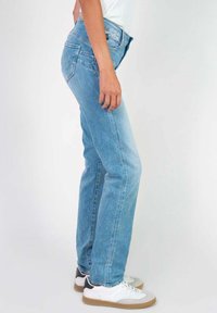 Jean droit bleu clair en denim, avec un design classique à cinq poches, porté avec des baskets blanches.