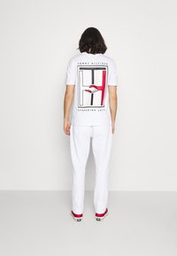 Vit bomullströja med en stor grafisk design på baksidan med röda, svarta och vita inslag. Matchas med vita byxor och sneakers.