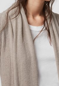 Cárdigan beige de canalé con un diseño de frente abierto, textura suave y corte relajado, superpuesto sobre una camiseta blanca.