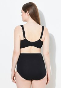 Zwarte bh met verstelbare bandjes en haaksluiting. Hoge zwarte onderbroek met een textuur banddetail. Gladde stof.